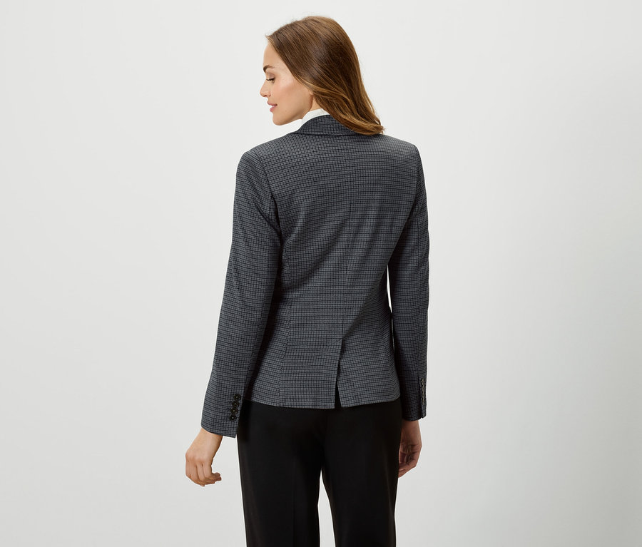 Žena má na sobě sako s kostkovaným vzorem a černé kalhoty.