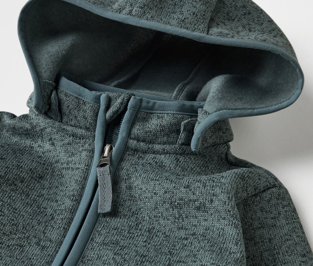 Detail dětského overalu z pleteného fleecu se zipem a kapucí.