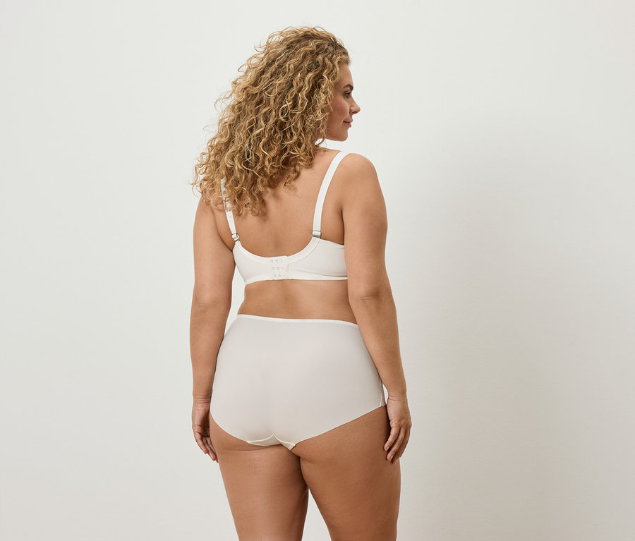 Zezadu: žena s kudrnatými vlasy má na sobě krémovou podprsenku a kalhotky.