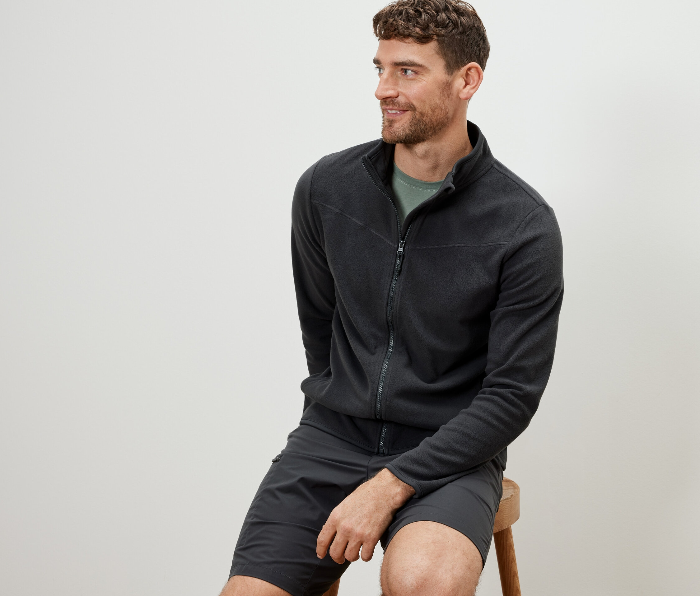 Muž sedí na stoličce a má na sobě antracitovou fleecovou bundu.