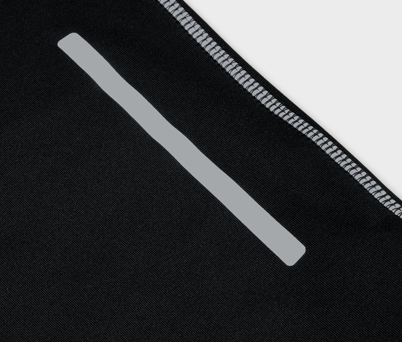 Detail černého sportovního oblečení s reflexním pruhem a šedým lemem.