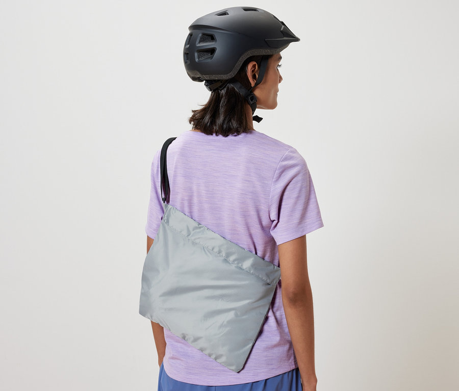 Žena s cyklistickou helmou má přes rameno přehozenou nákupní tašku na kolo.