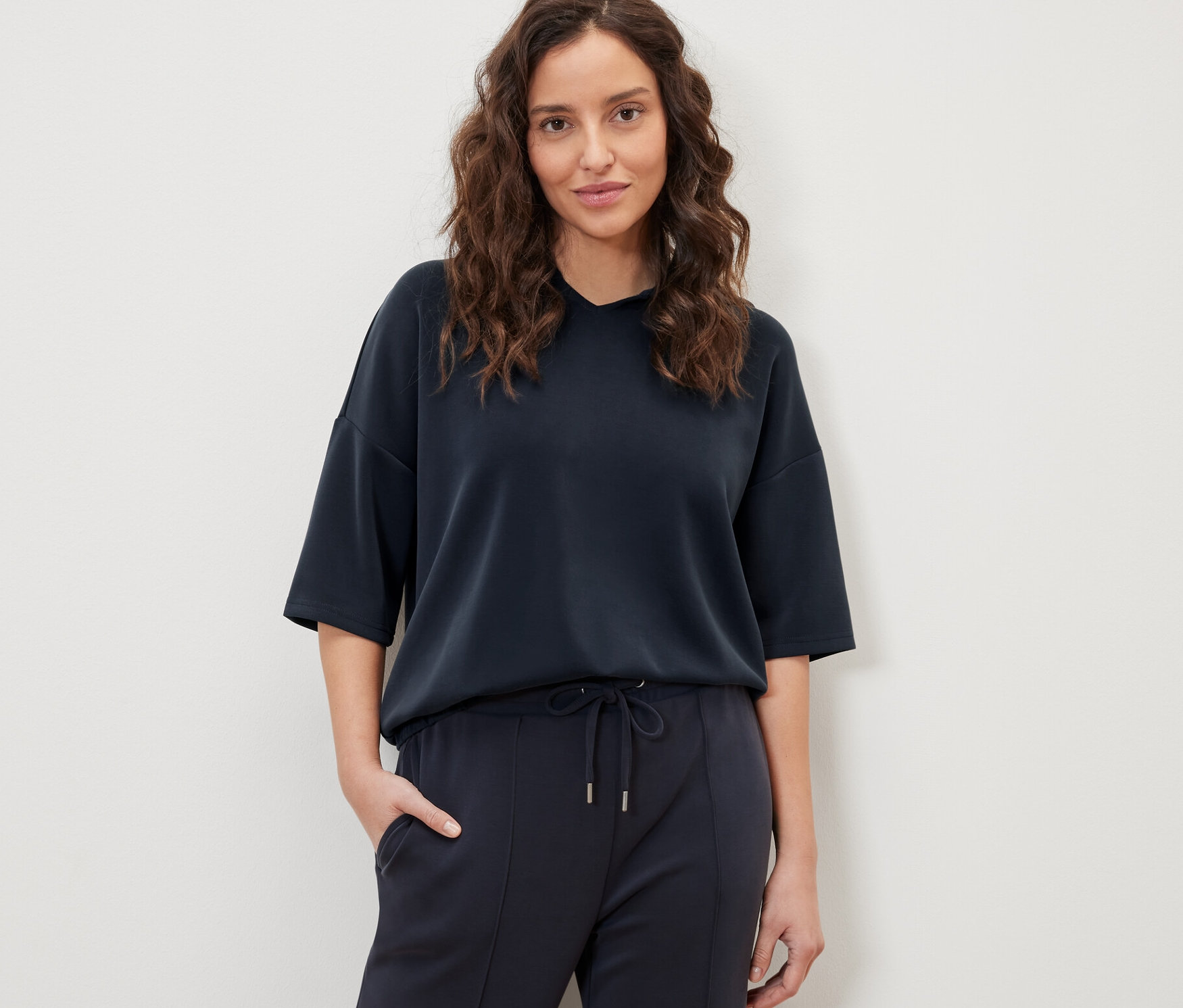 Žena pózuje v tmavě modré mikině s kapucí z modalové směsi a kalhotách.