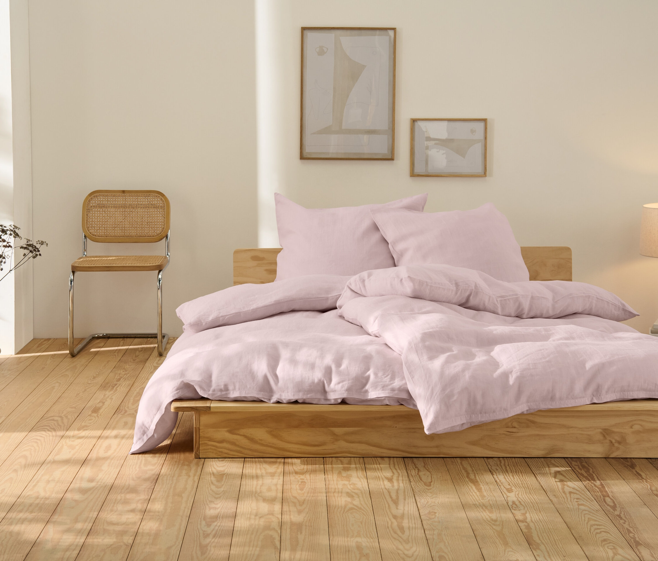 Na dřevěné posteli je růžové lněné povlečení nadměrné velikosti.