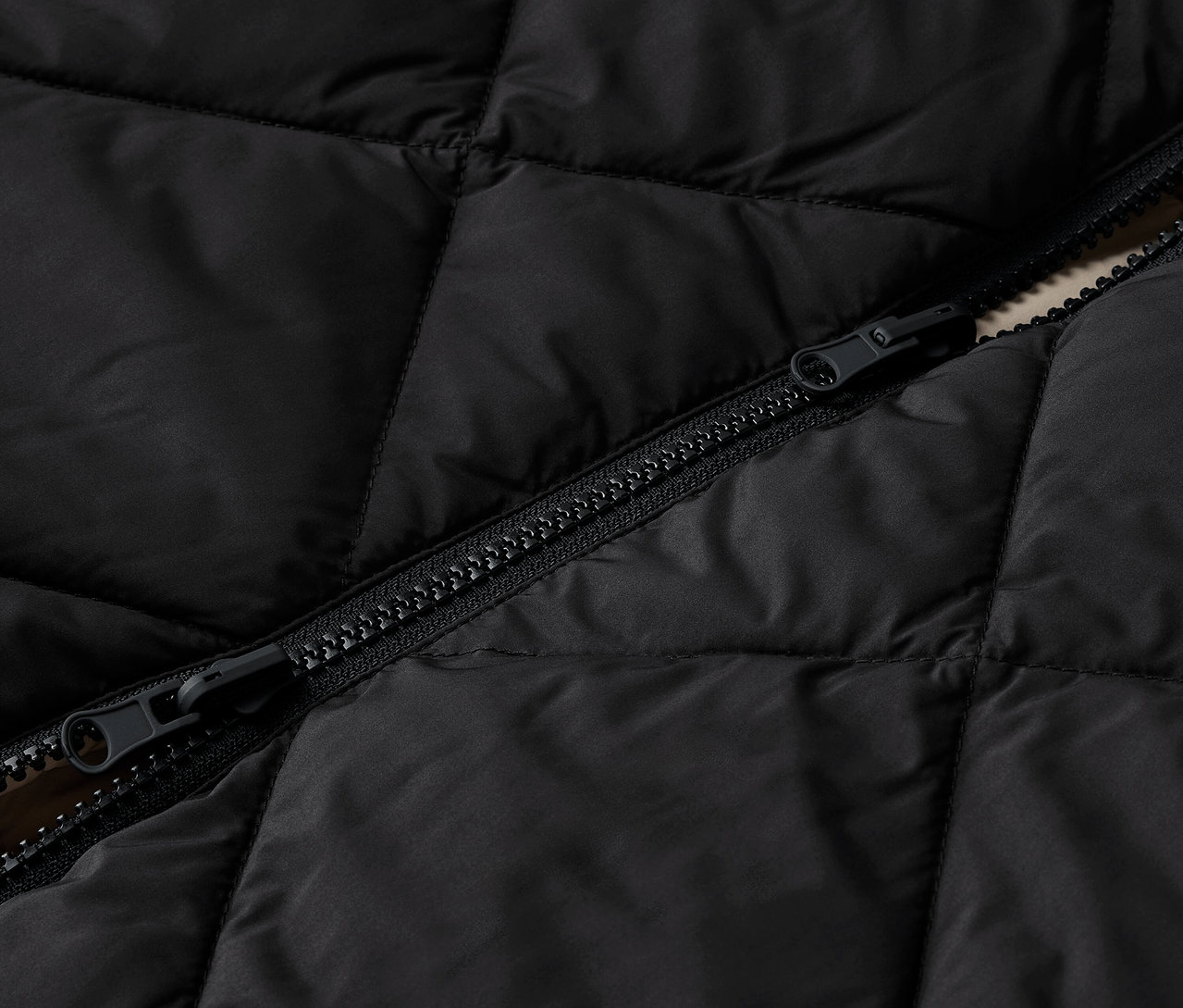 Detail černé prošívané bundy se zipem.