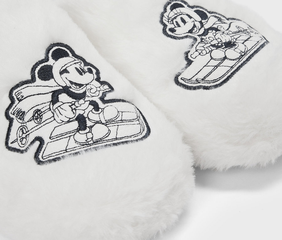 Detail bílých chlupatých pantoflí s kreslenými obrázky Mickey Mouse na saních.