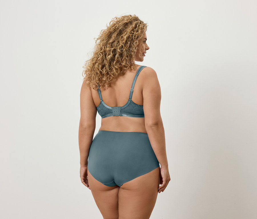Pohled zezadu na ženu s vlnitými vlasy v modrozelené podprsence a kalhotkách.