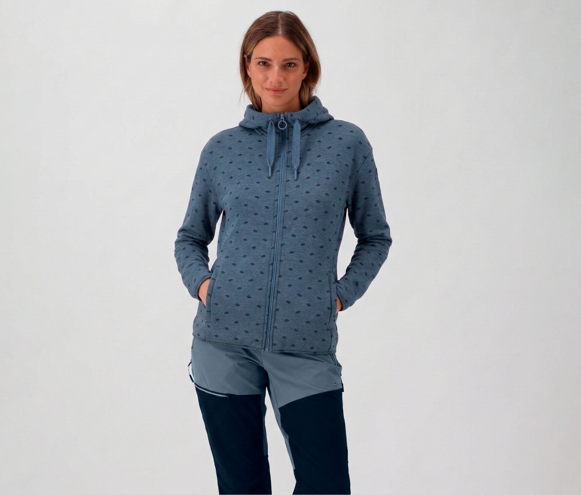 Žena s kapucí a modrá dámská fleecová bunda s kapucí CMP s rukama v kapsách.