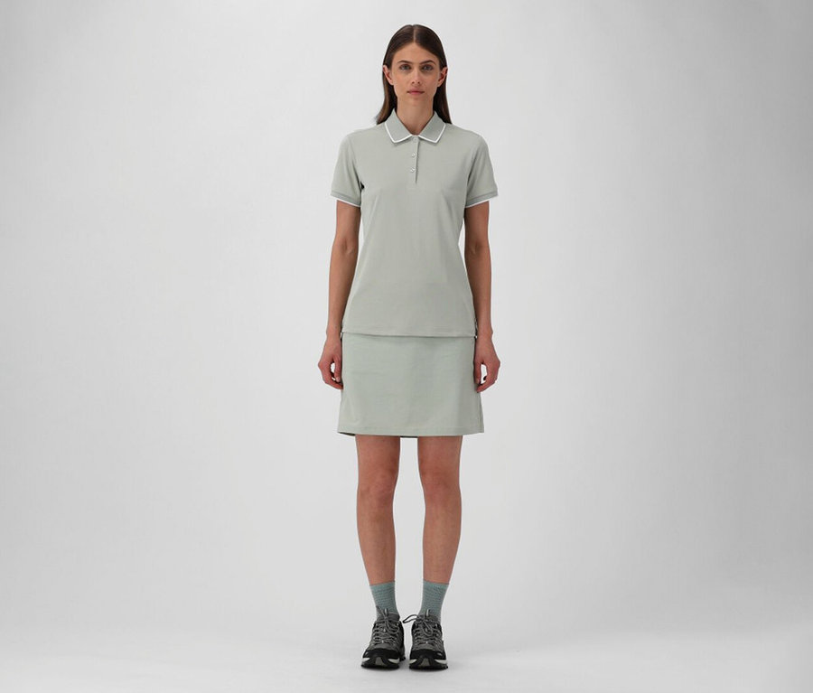 Žena v dámské outdoorové sukni CMP a pistáciové dámské polokošili ze strečového piké CMP, šedé ponožky a trekové boty.