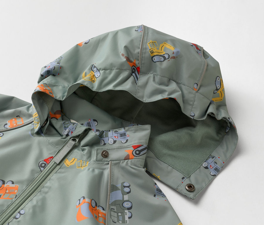 Detail olivově zelené dětské bundy s kapucí, potištěné stavebními vozy.