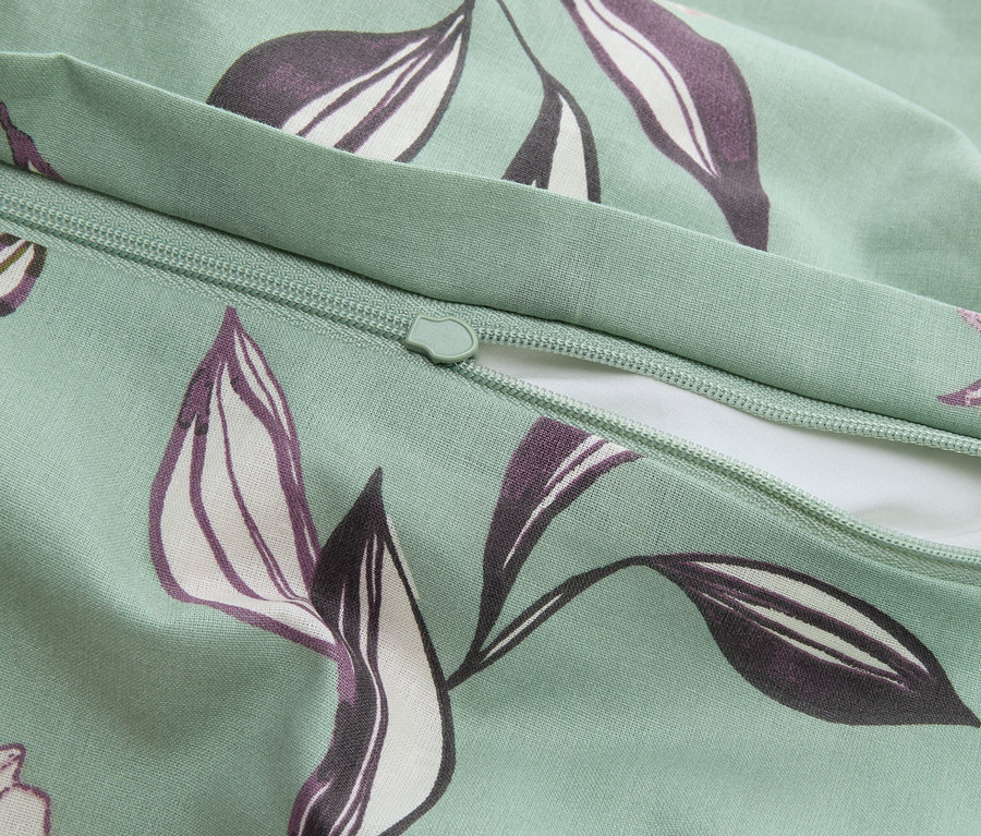 Detailní záběr mátově zeleného povlaku na polštář se zipem a fialovým vzorem listů.