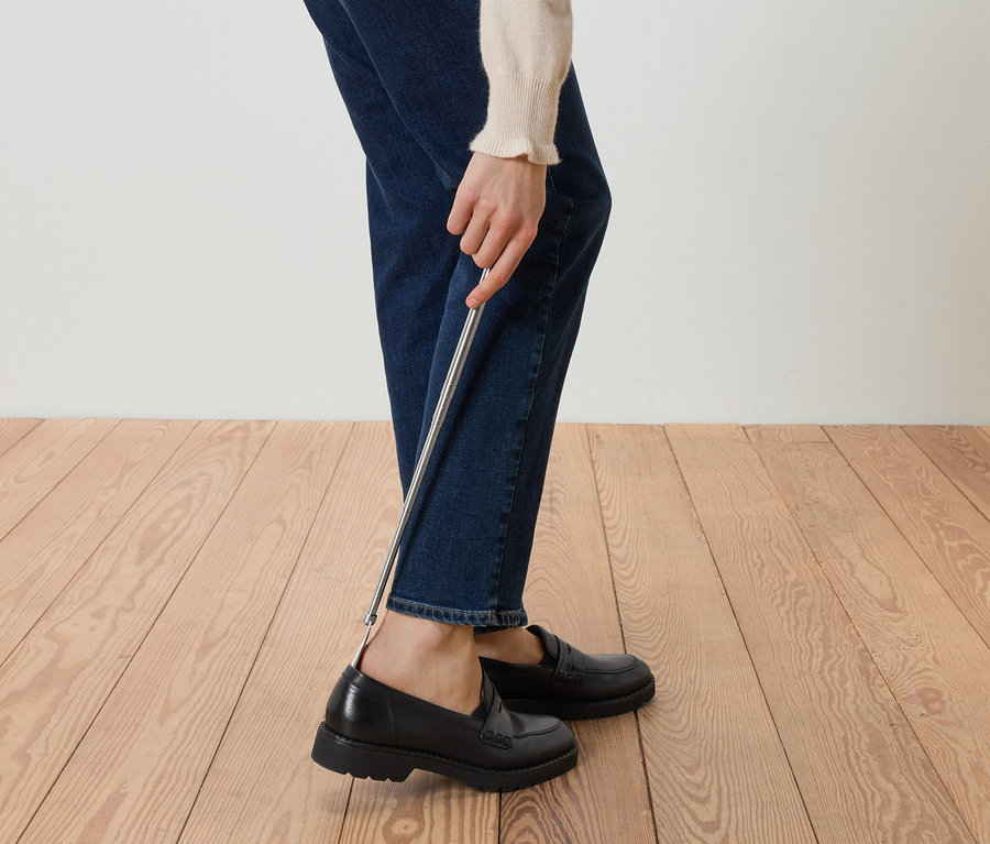Osoba si obouvá černé mokasíny pomocí obouvátka.