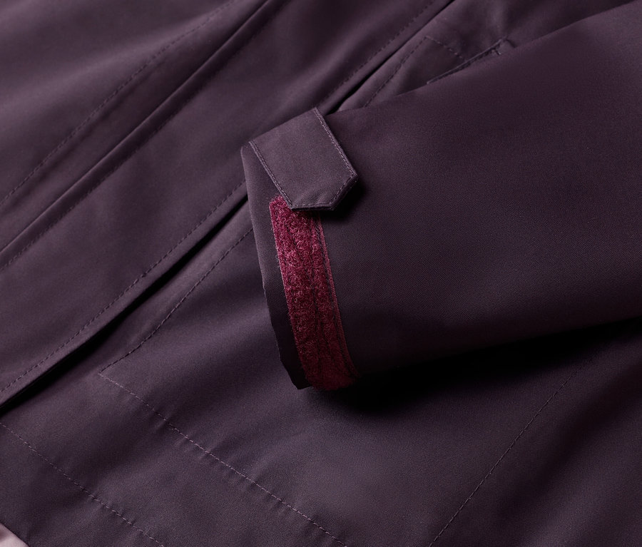 Detailní záběr na lilek bundu s knoflíkem na rukávu a vínovým akcentem.