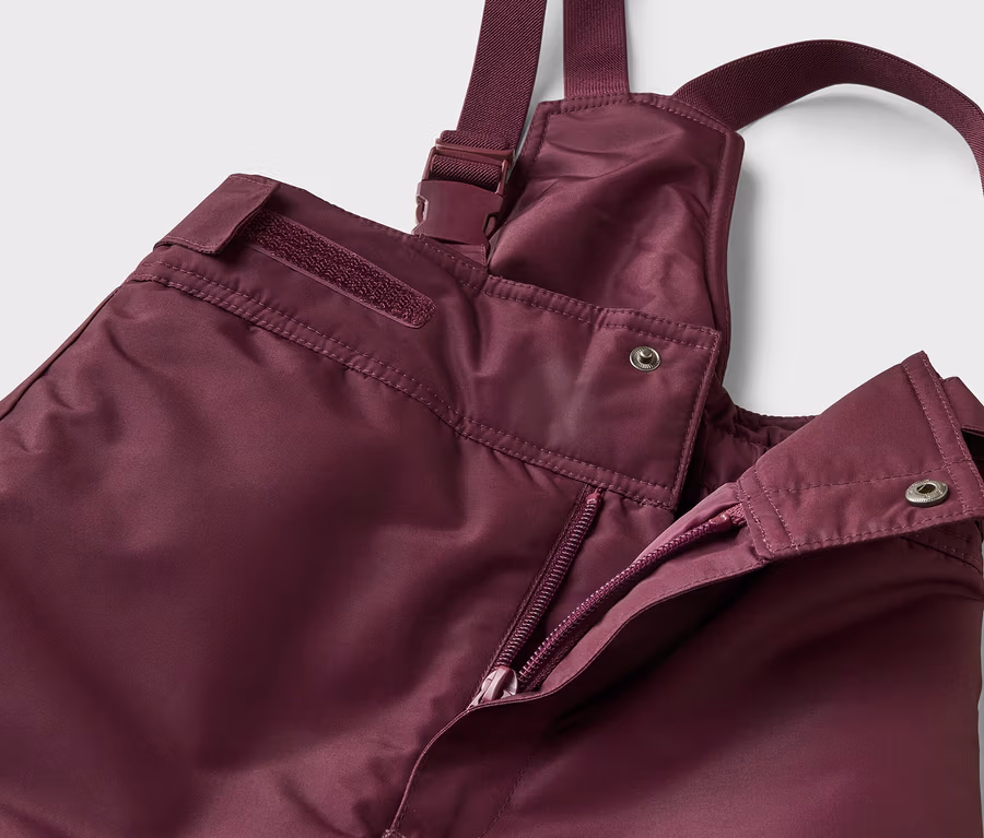 Detailní záběr na otevřené lilek kalhoty s laclem se zipem a knoflíky na bílém pozadí.