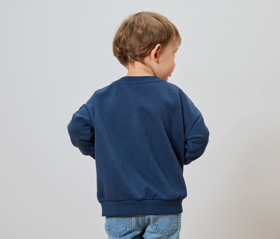 Chlapec s blond vlasy má na sobě tmavě modrou mikinu a džíny.