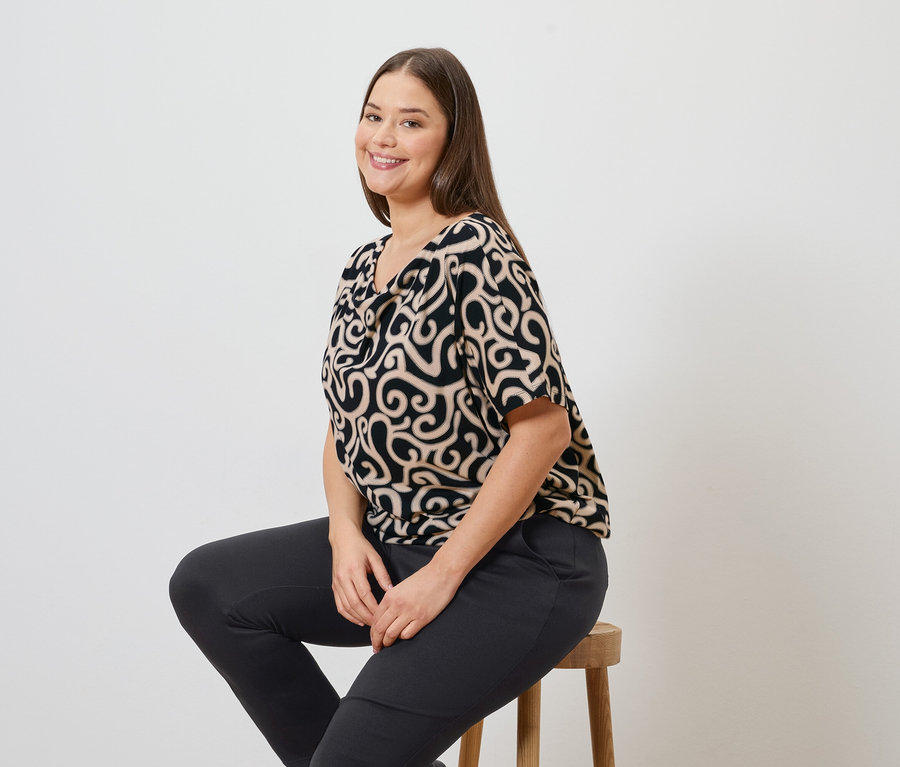 Žena sedí na stoličce a má na sobě vzorovanou blůzu a kalhoty joggpant.