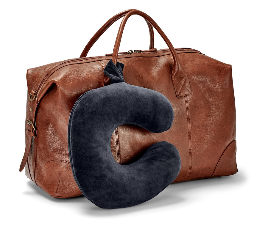 Tmavě modrý cestovní polštář visí před hnědou cestovní taškou.