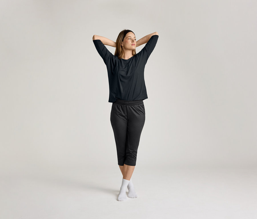 Žena se spojenýma rukama za hlavou má na sobě černé 3/4 sportovní triko.