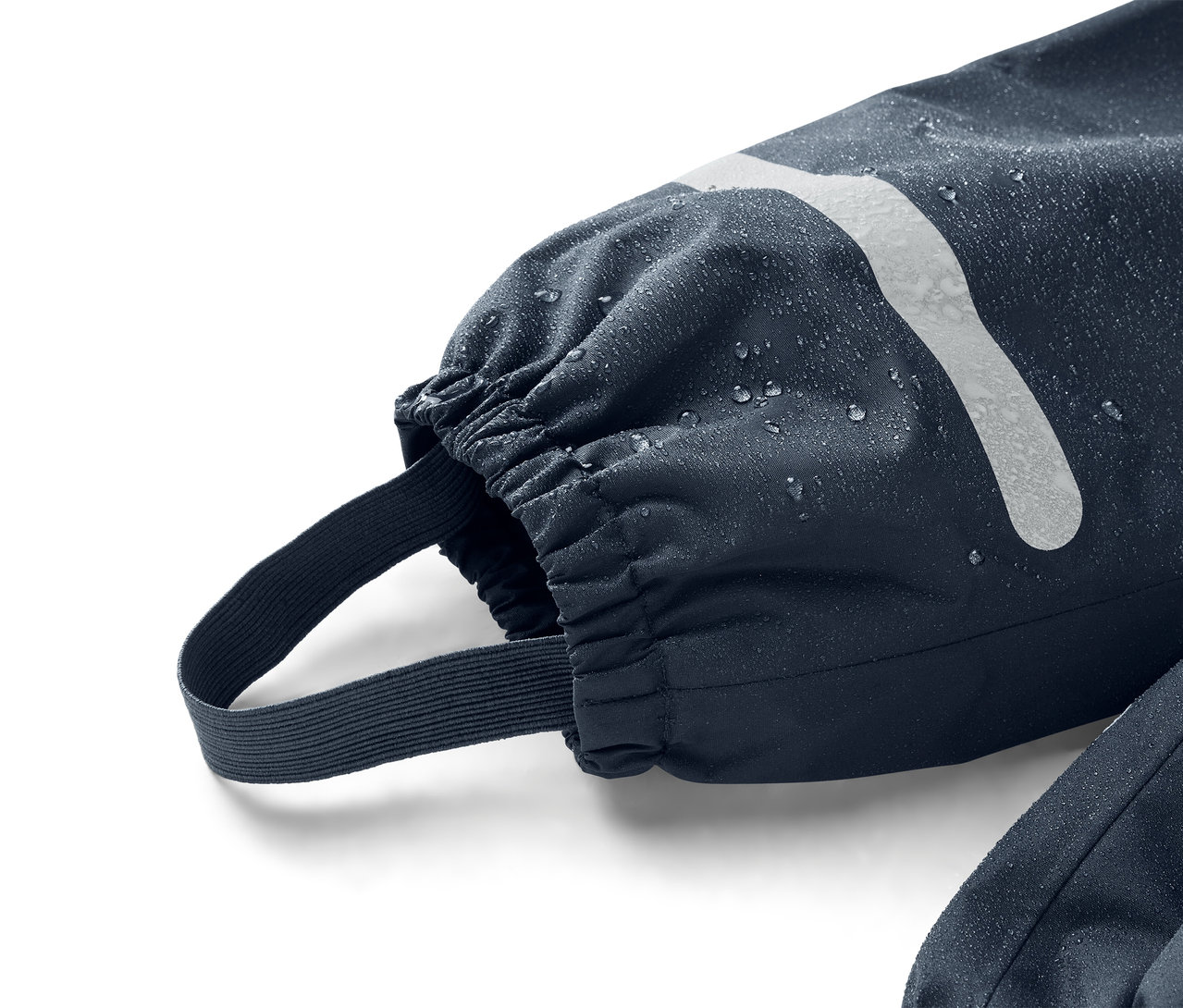 Detailní záběr na tmavě modrý rukáv s elastickou manžetou a páskem přes chodidlo, pokrytý kapkami vody.