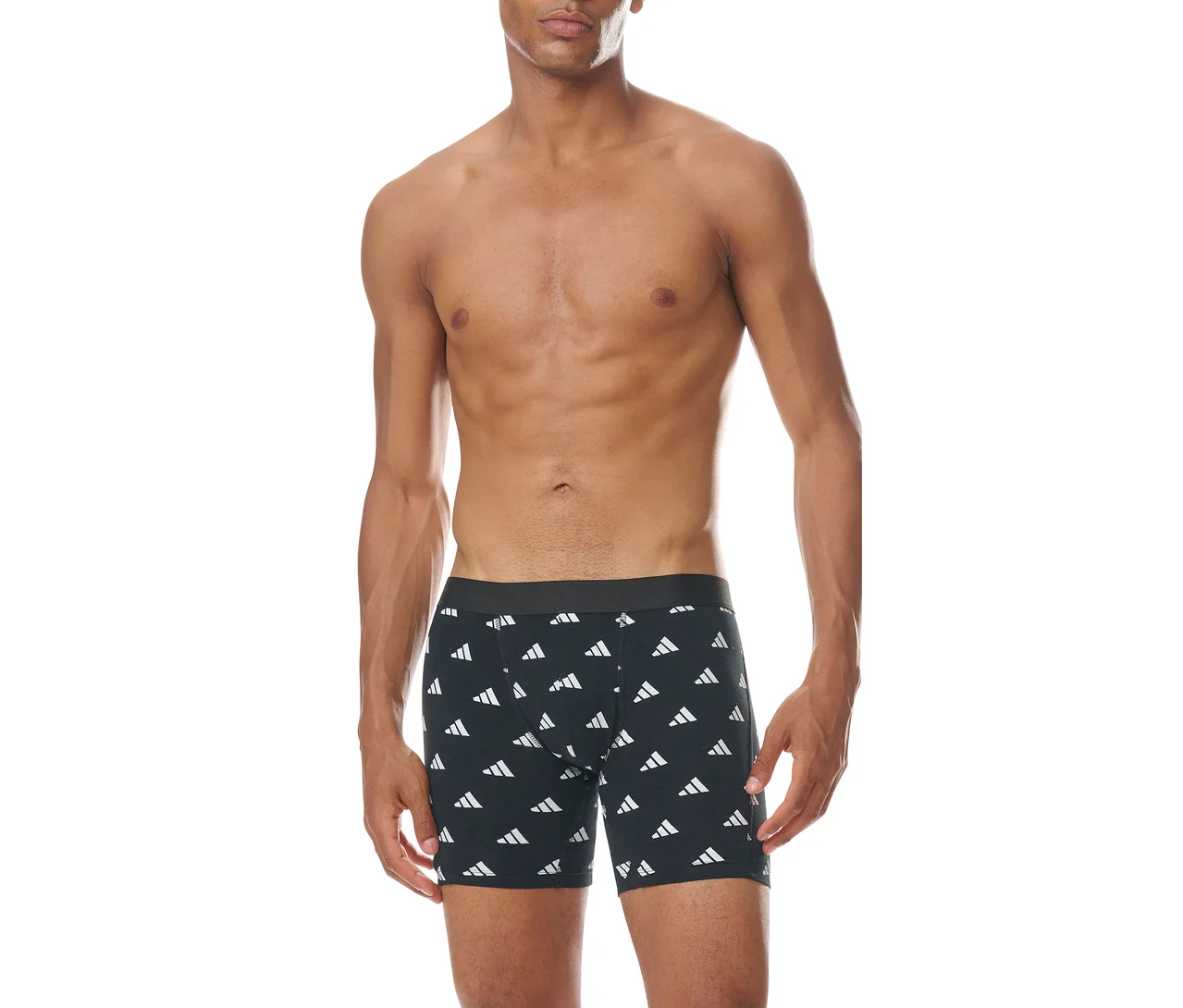 Muž bez trička stojí čelem, oblečený v černých boxerkách s opakujícím se bílým vzorem loga Adidas.