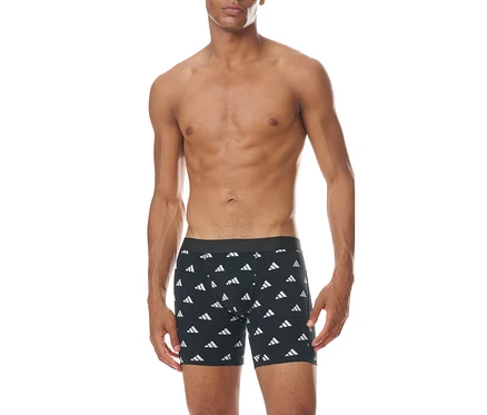 Muž bez trička stojí čelem, oblečený v černých boxerkách s opakujícím se bílým vzorem loga Adidas.