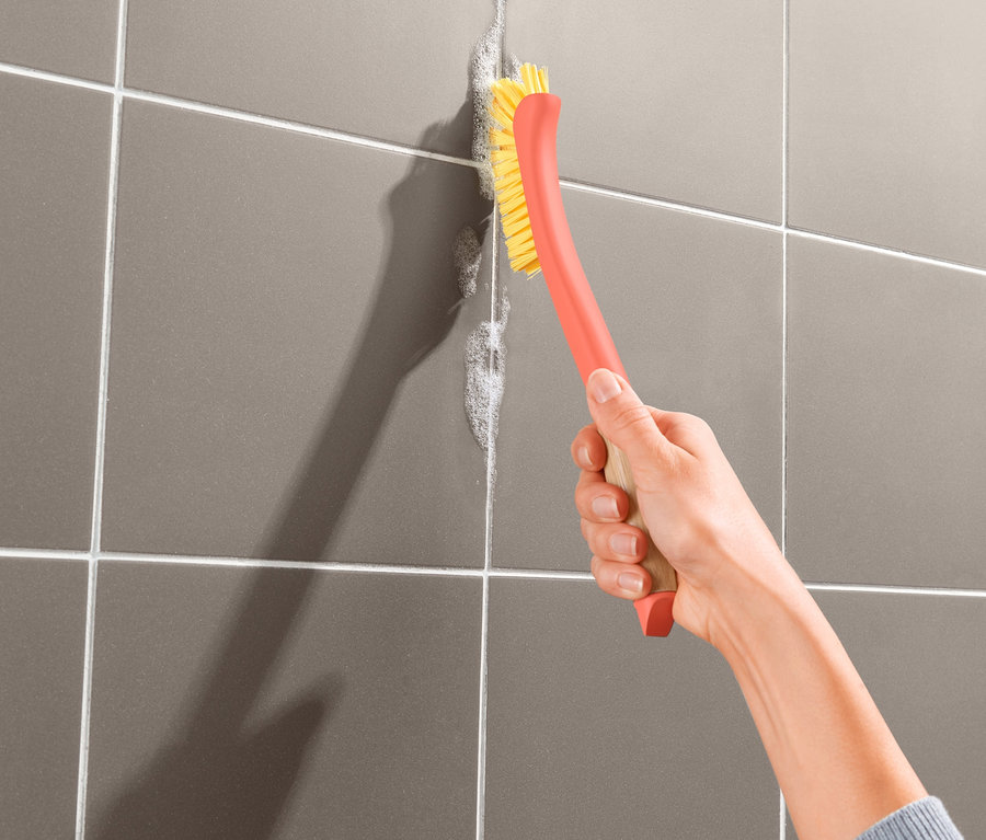 Žena čistí spáry mezi dlaždicemi kartáčem na čištění spár.