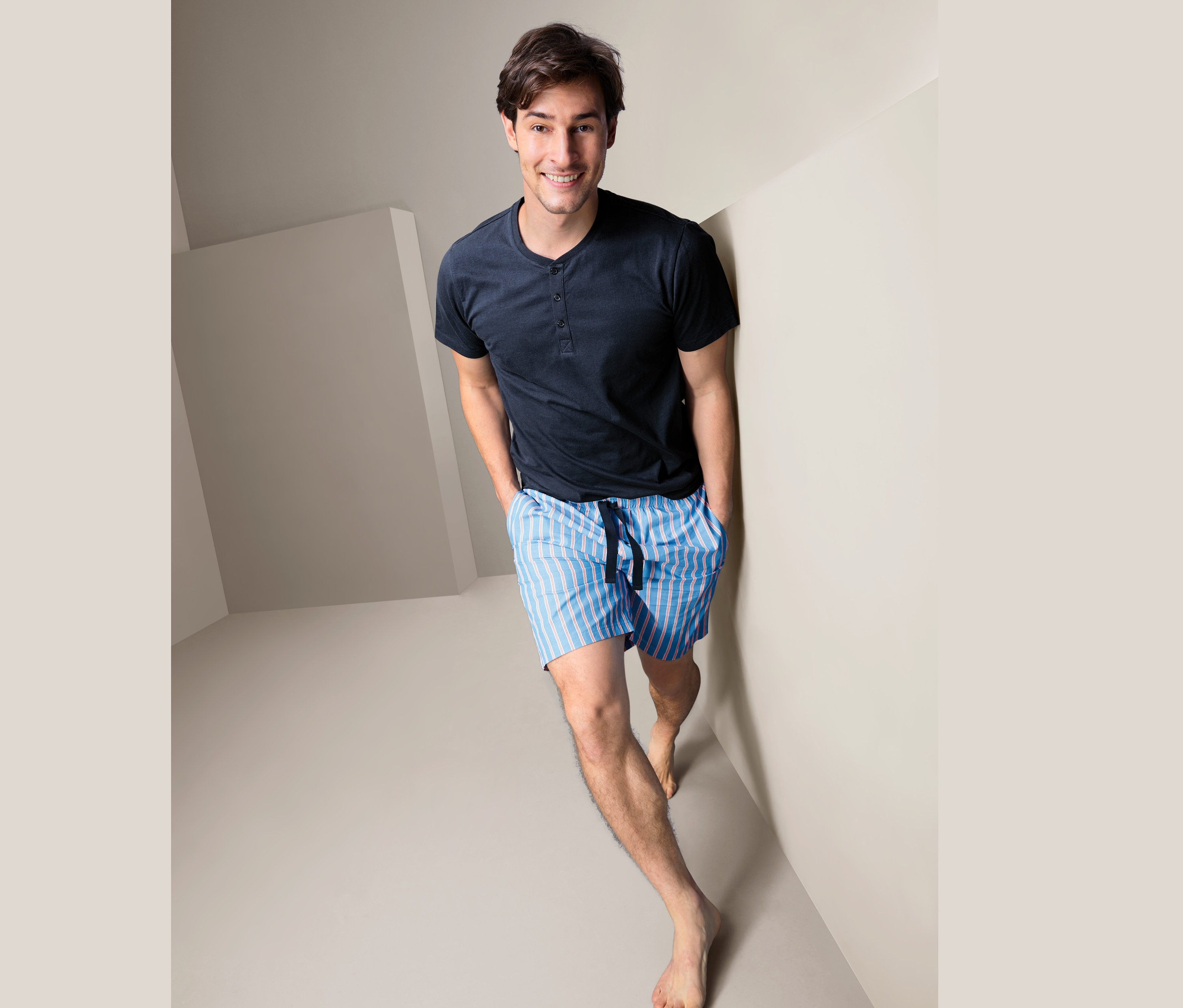 Muž v krátkém pyžamu stojí v rohu místnosti.