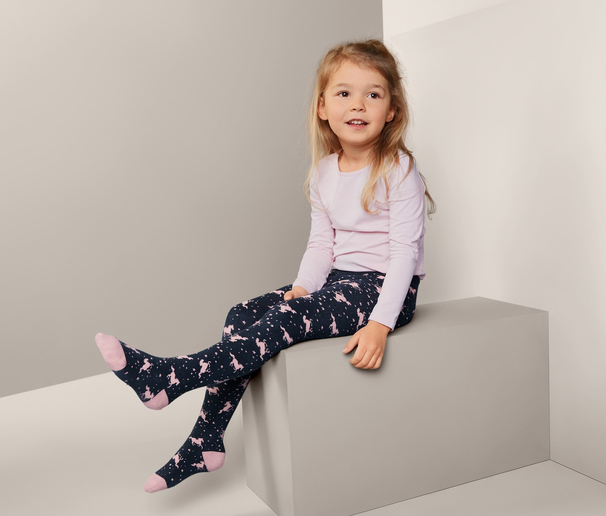 Dívka sedí a má na sobě termopunčocháče se vzorem jednorožců, 2 páry.