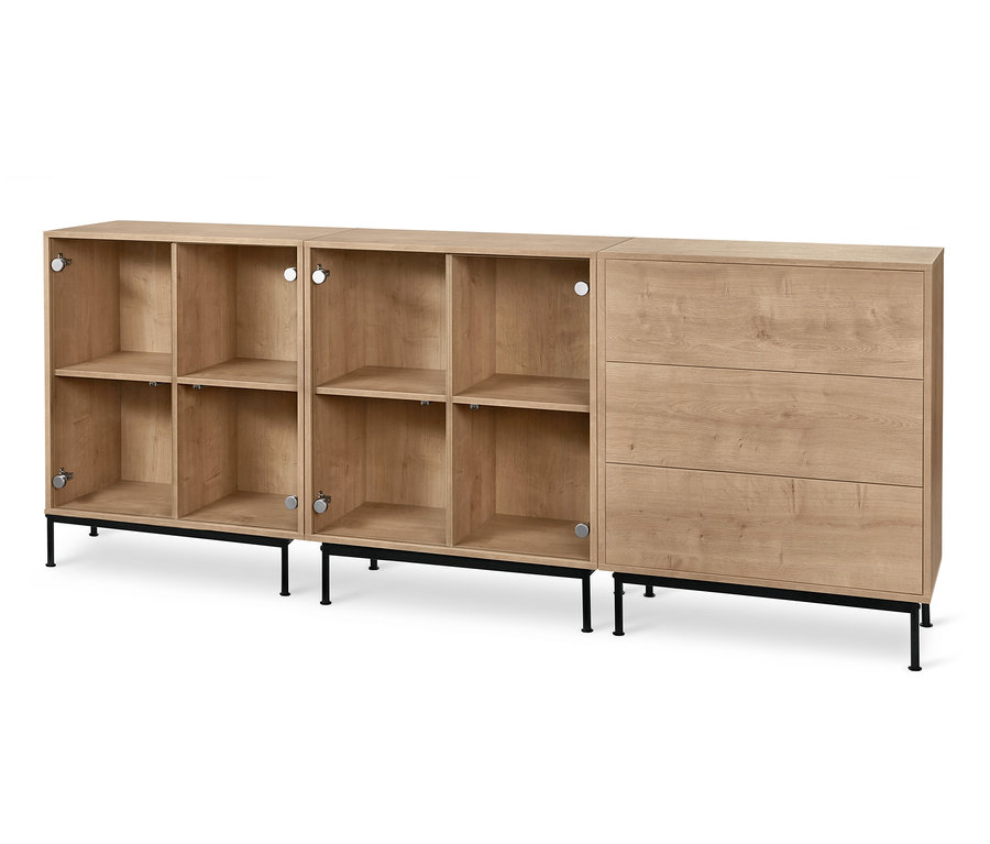 Dva regálové moduly »Flemming« se skleněnými dvířky a jeden se třemi zásuvkami v dubovém dekoru stojí na černém kovovém podnoží »Flemming«.