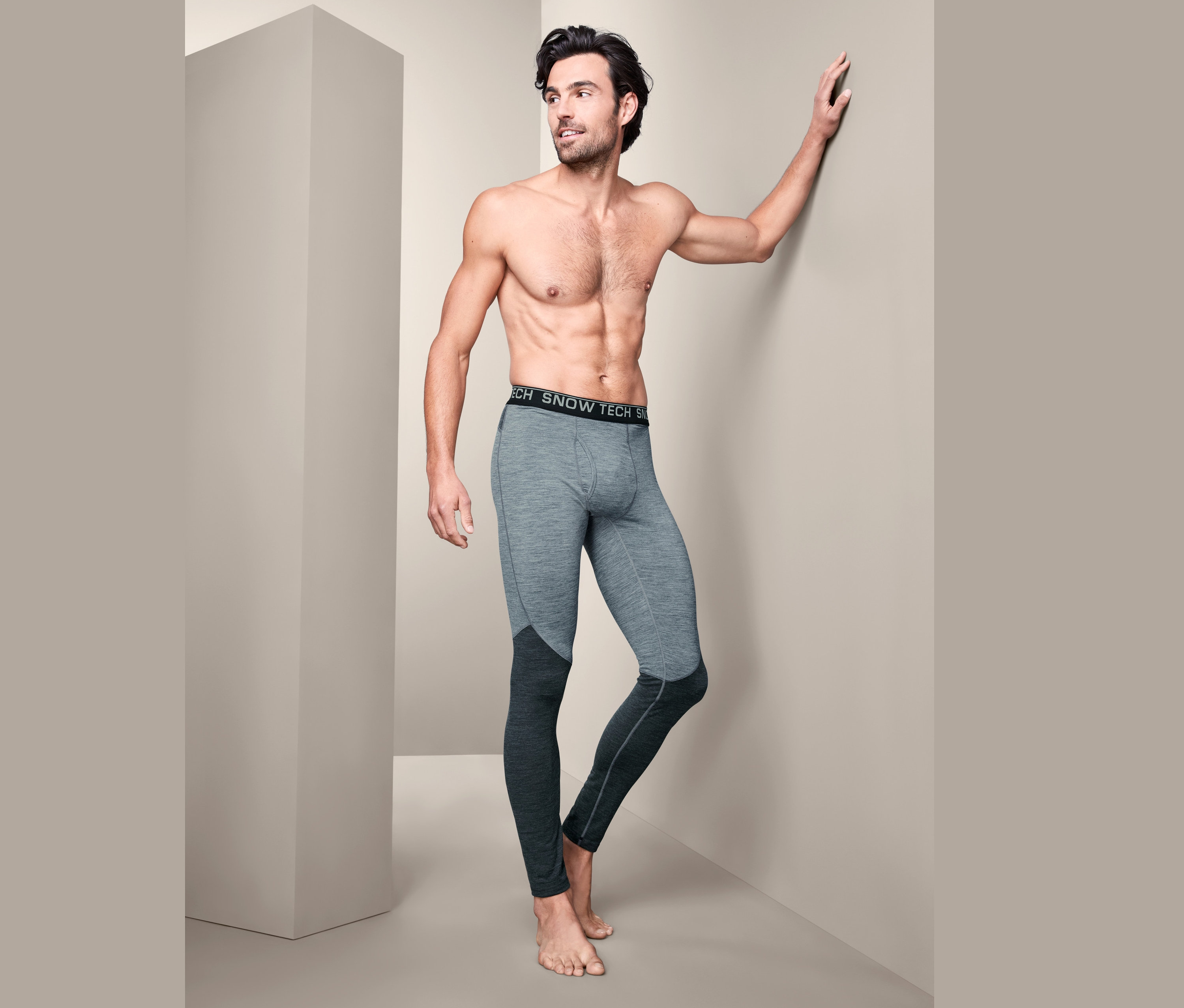 Muž bez trička pózuje v šedých funkčních spodkách s vlnou merino.