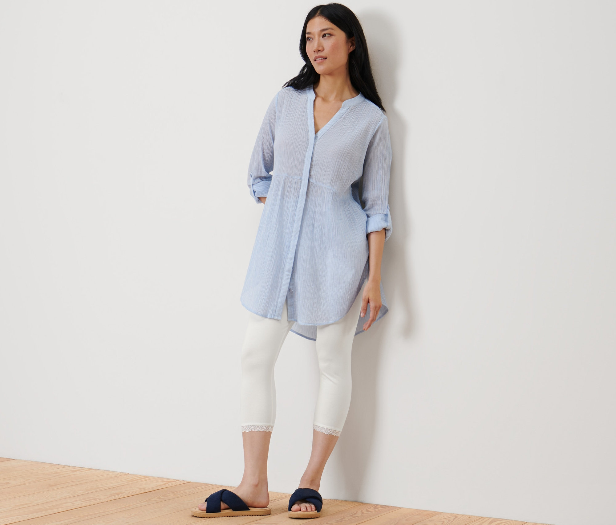 Žena stojí opřená o zeď a má na sobě 3/4 bílé legíny s krajkovým lemem.