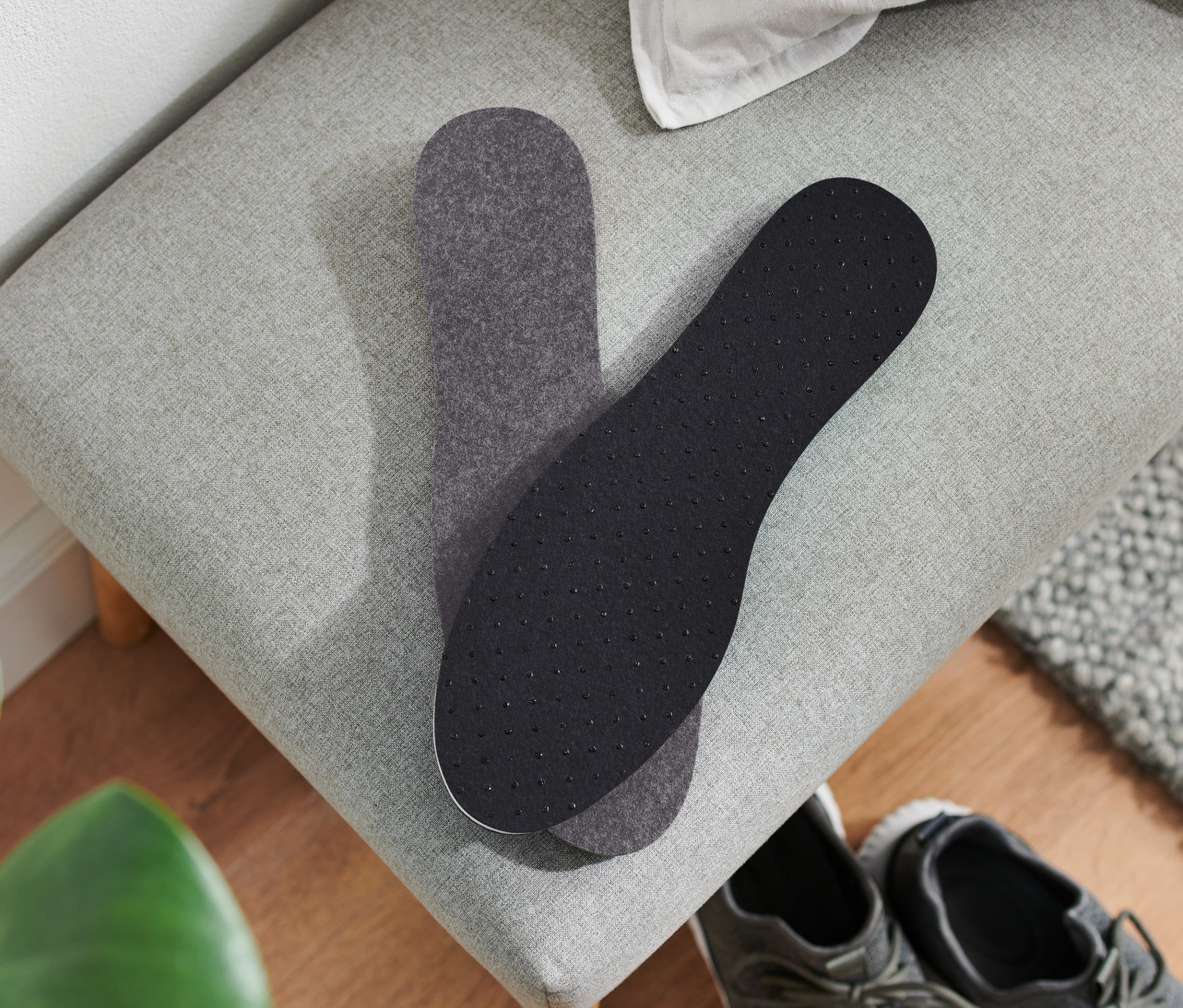 Dvě termoizolační vložky do bot leží na šedé lavici vedle páru šedých bot.