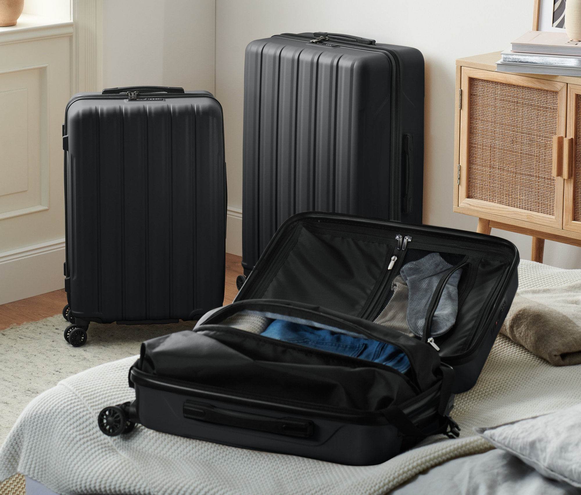 Tři černé kufry z tvrdé skořepiny, jeden malý otevřený na posteli.