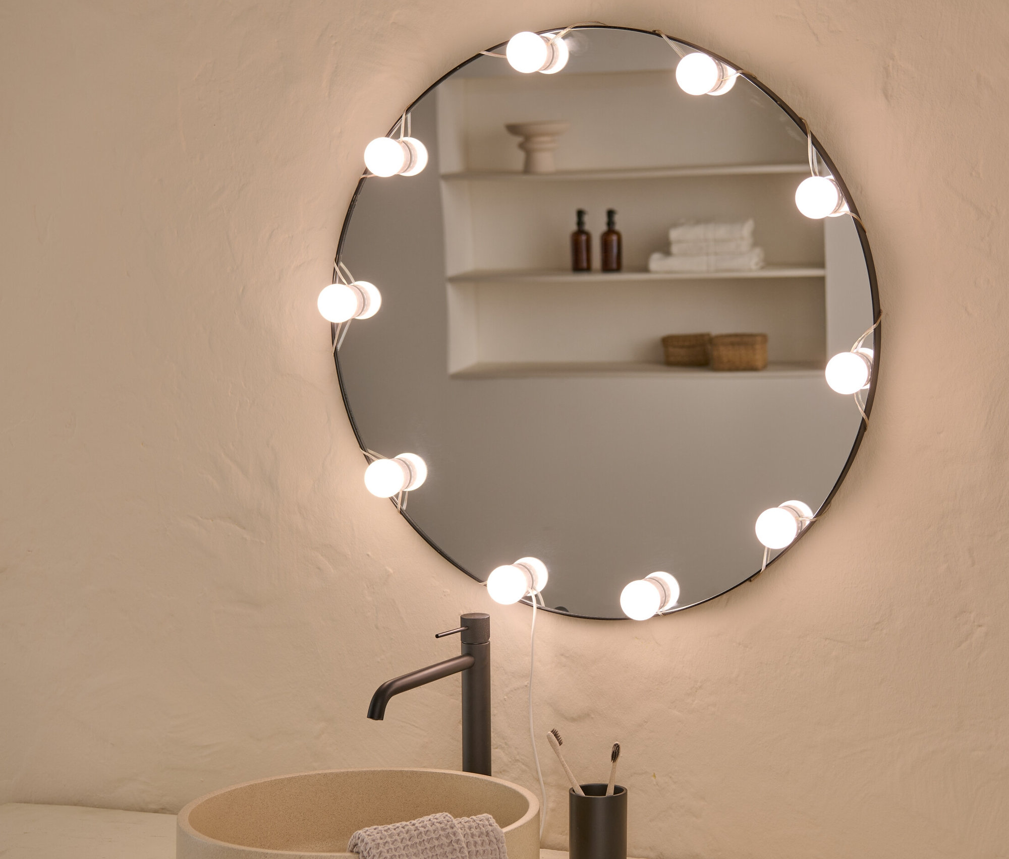 Koupelna s umyvadlem, baterií a kulatým zrcadlem s LED světelným řetězem s USB.