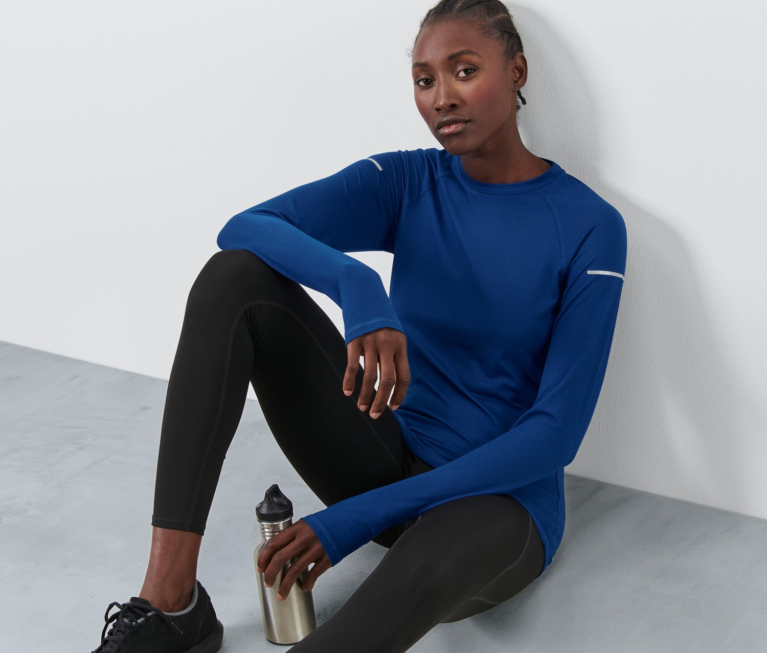 Žena sedí na podlaze a má na sobě modré funkční tričko s dlouhým rukávem.