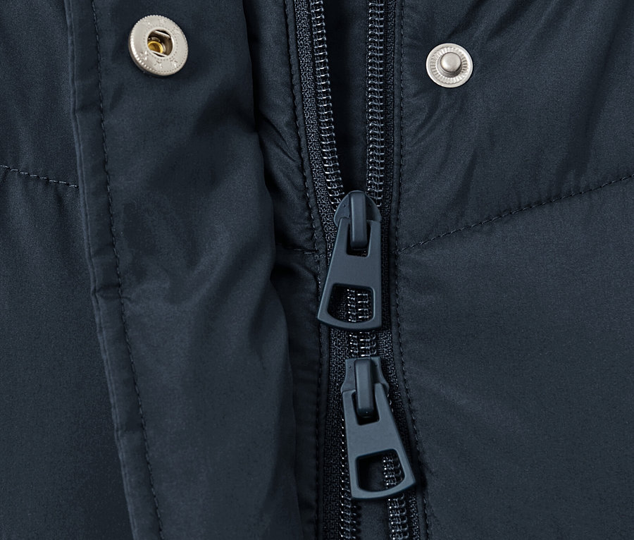 Detail tmavě modré prošívané bundy s kapucí zobrazuje zip a patentky.