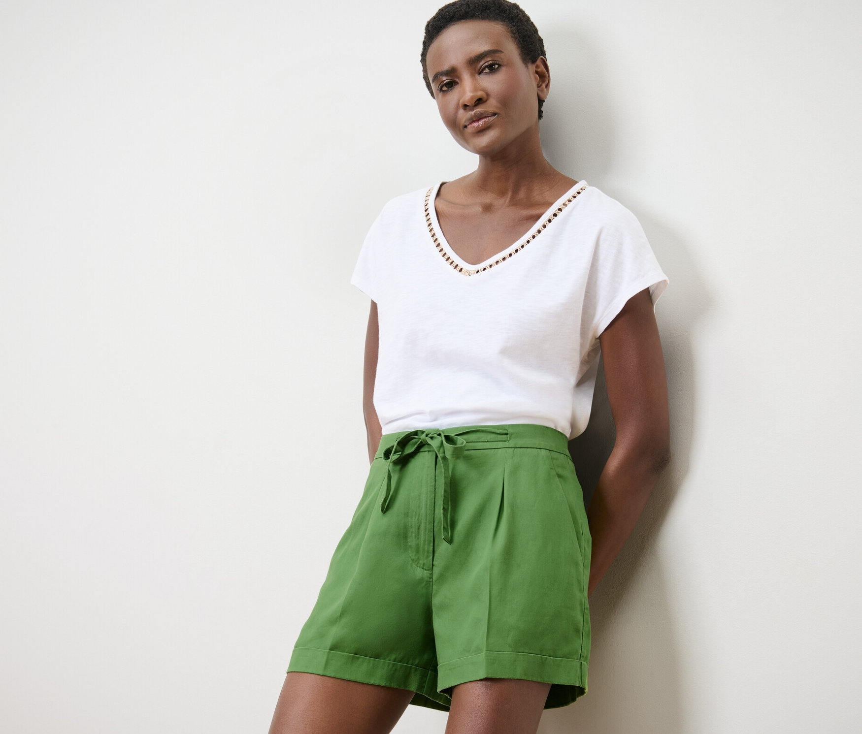 Žena pózuje v zelených lněných šortkách a bílém tričku.