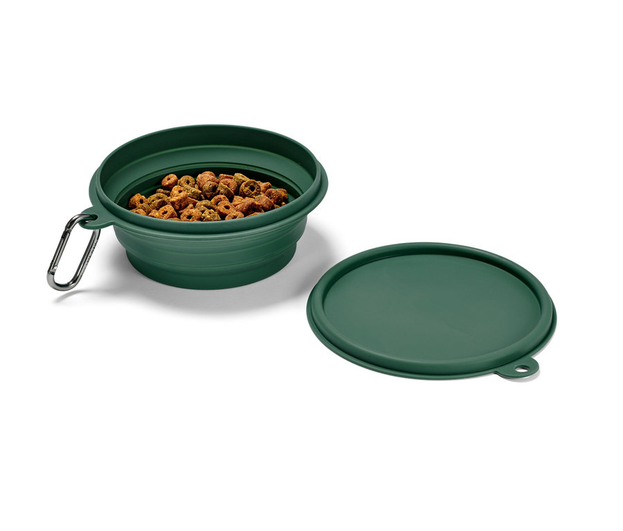 Zelená skládací miska na krmivo s karabinou, naplněná granulemi, vedle leží víčko.