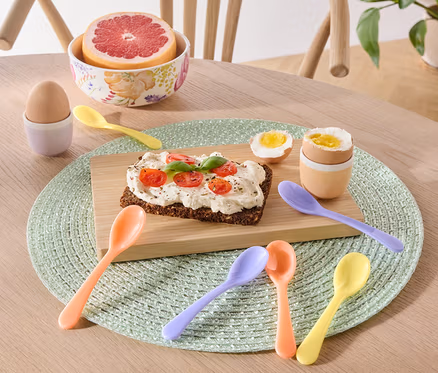 Na stole leží talíř s toastem, vajíčkem a grapefruit a sada 6 lžiček na vajíčka.