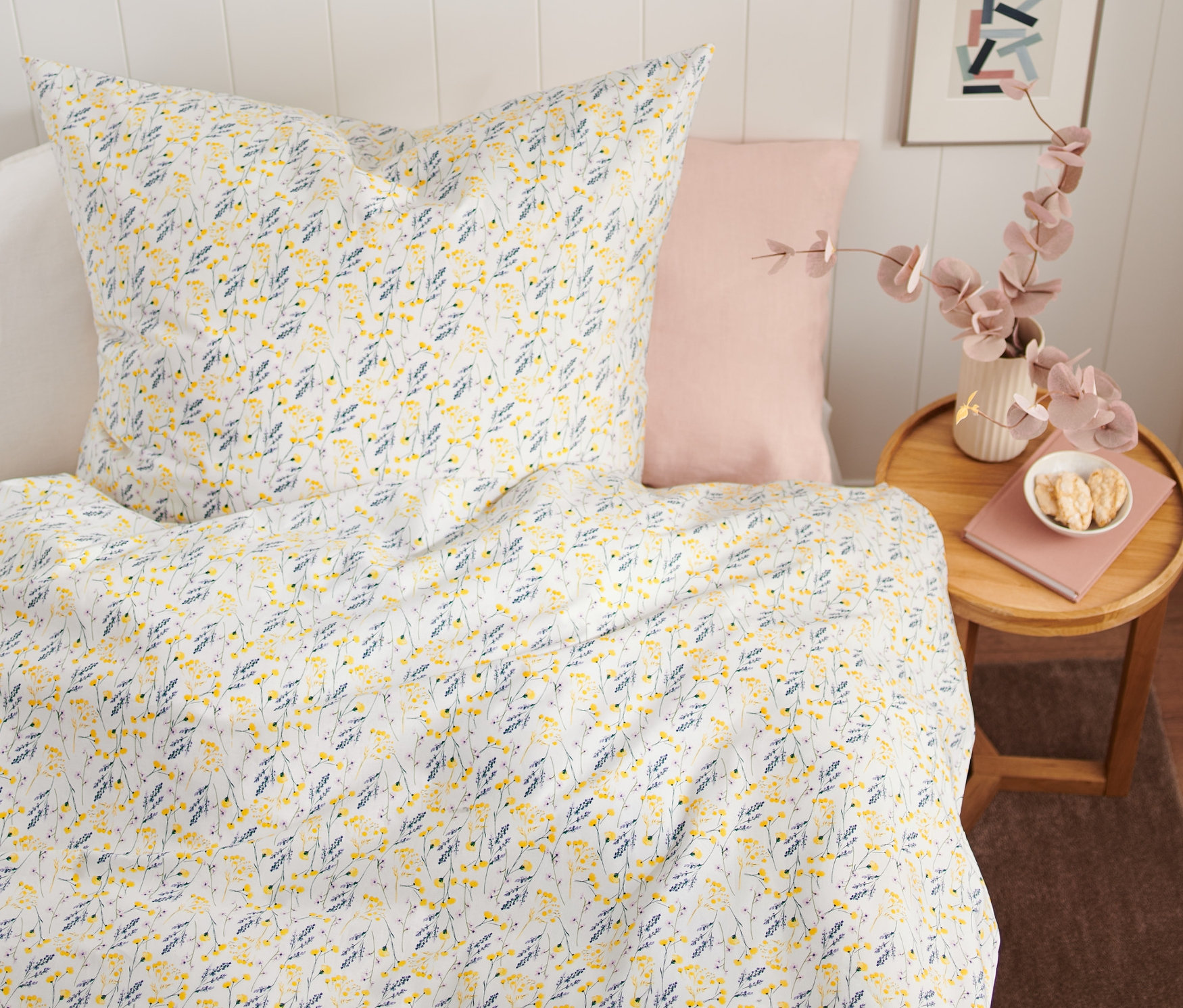 Květinový vzor na prémiovém bavlněném povlečení standardní velikosti na posteli. Vedle postele stojí stolek s vázou a knihou.