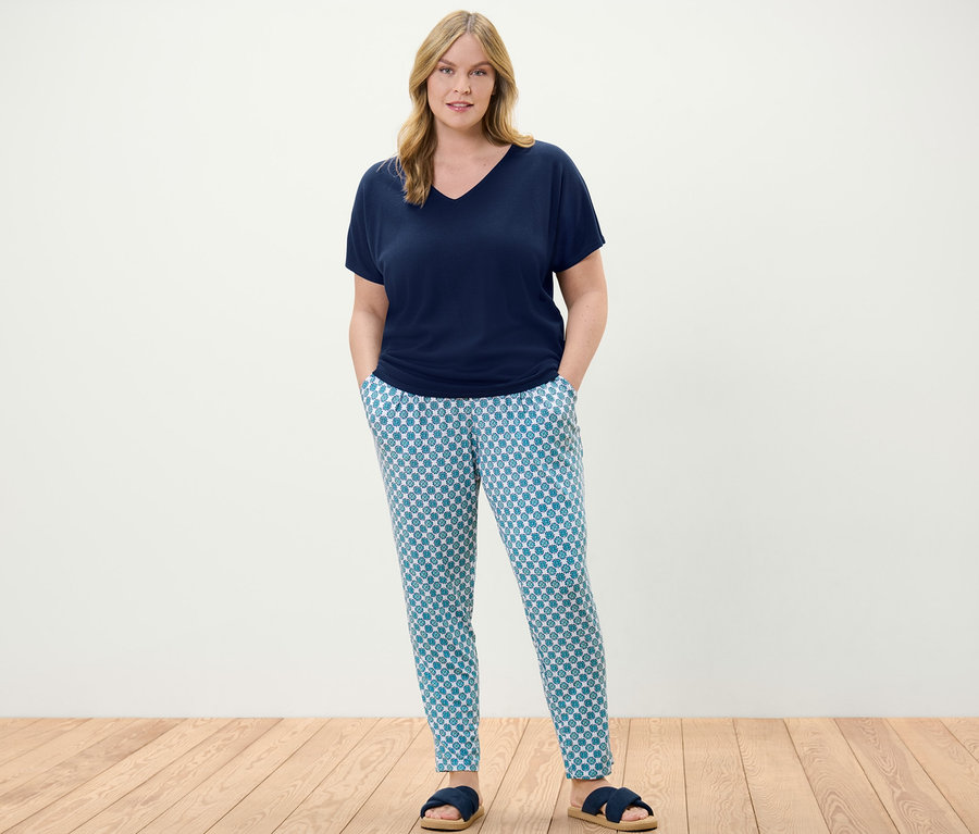 Žena stojí a má na sobě tmavě modré strukturované tričko a žerzejové kalhoty s celoplošným potiskem.