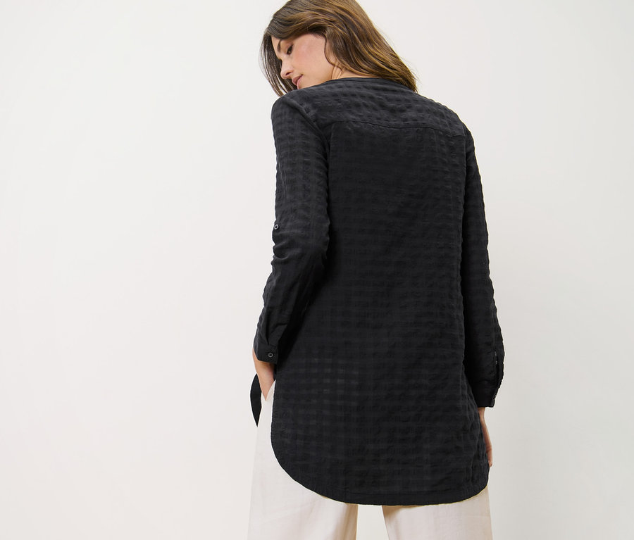 Žena má na sobě dlouhou tuniku s tkanou strukturou a kalhoty.