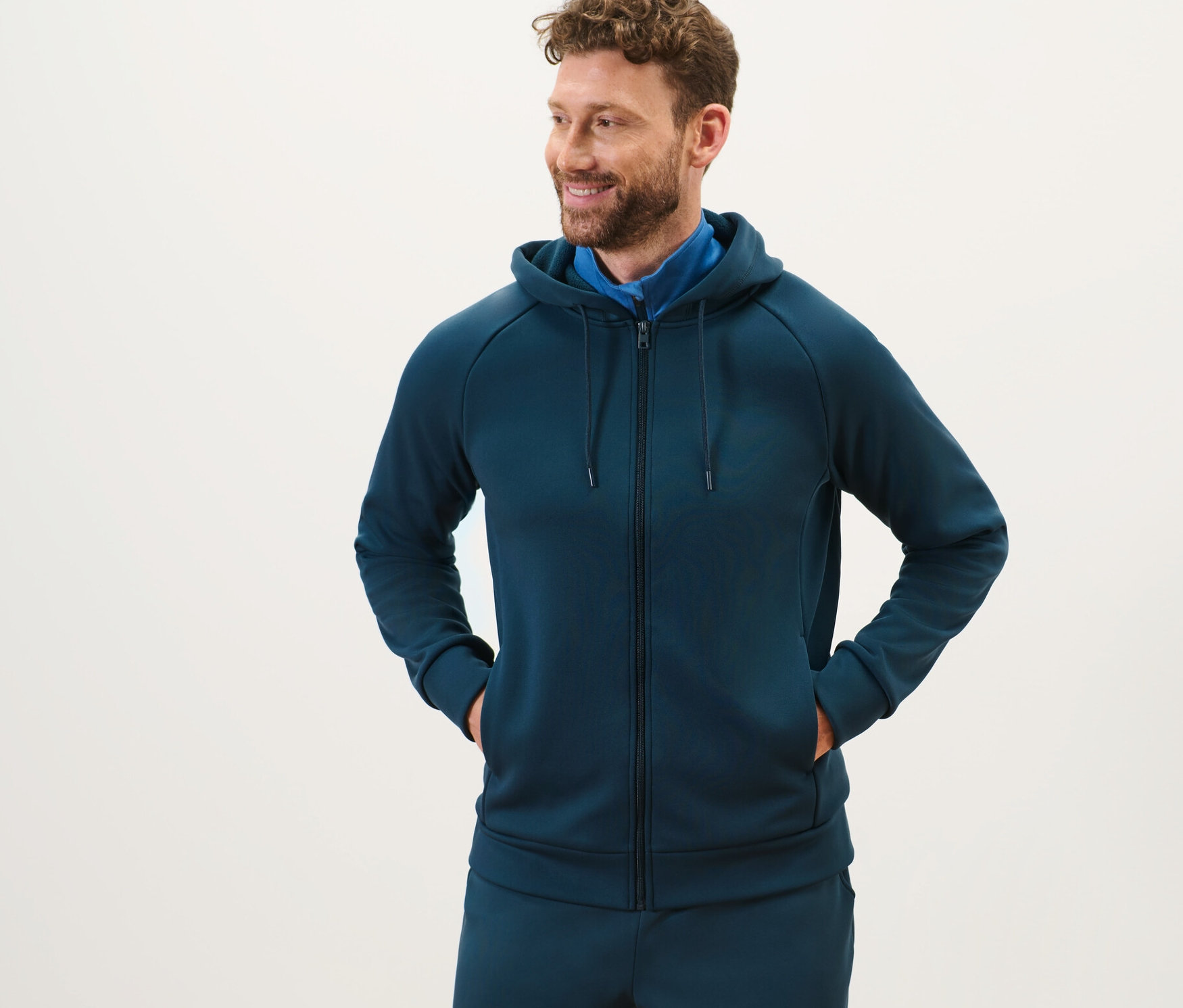 Muž s vousy stojí a má na sobě funkční bundu s kapucí.