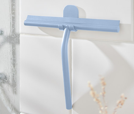 Modrá koupelnová stěrka s nástěnným držákem na bílých dlaždicích vedle sprchy.