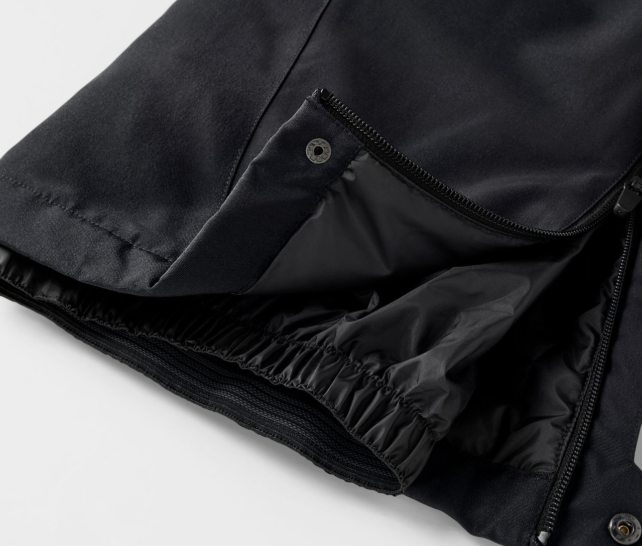 Detail černých kalhot s rozepnutým zipem a patentkou.