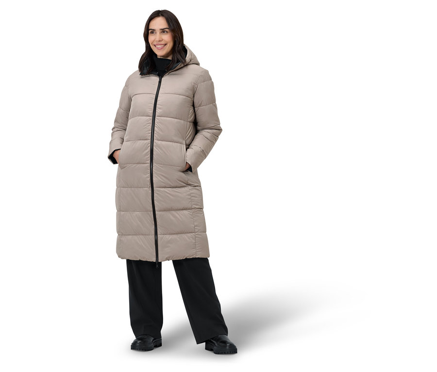 Žena pózuje v béžovém péřovém kabátě a černých kalhotách.