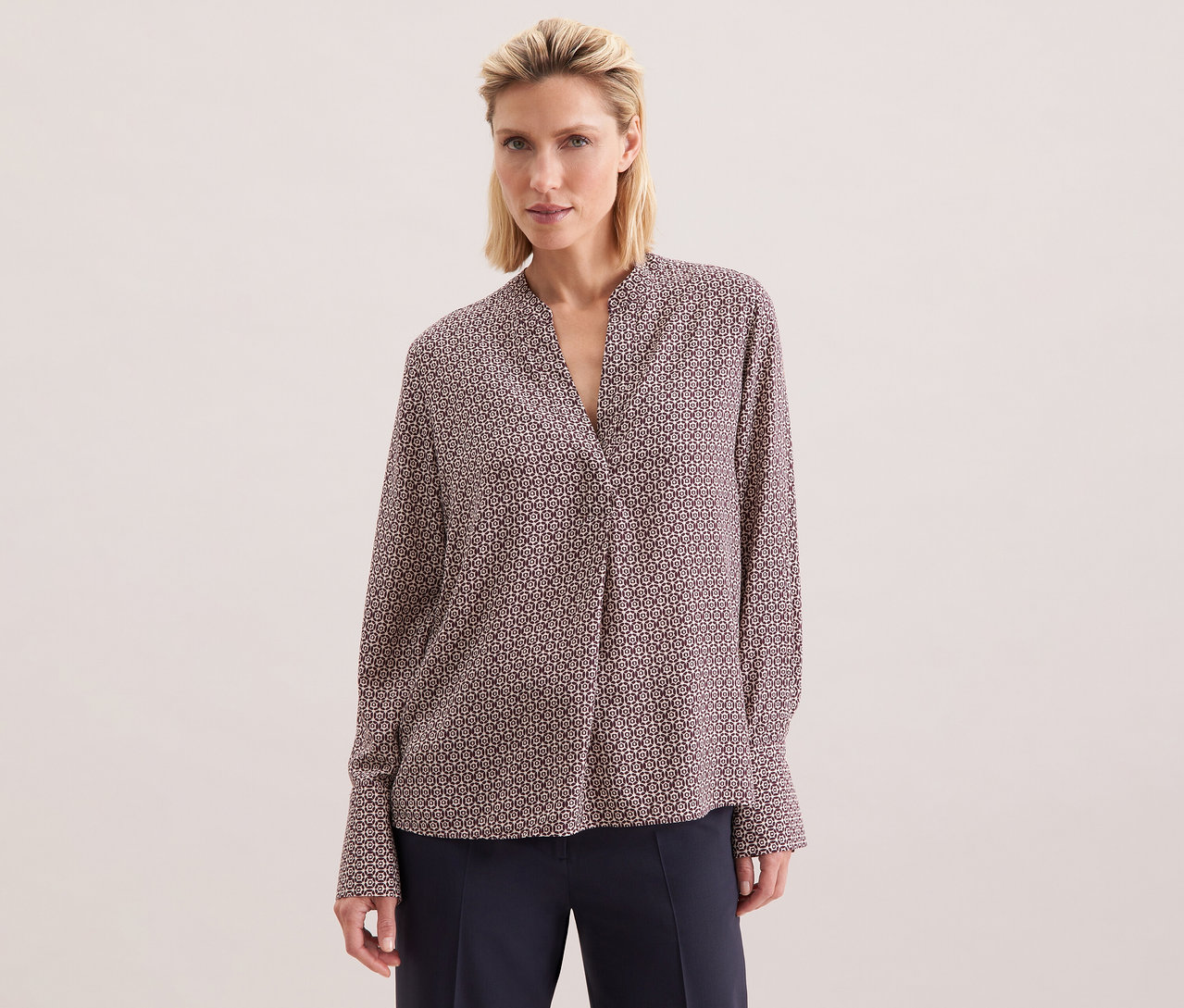 Žena má na sobě tuniku z viskózy Seidensticker s celoplošným potiskem v barvě ecru a burgundské.