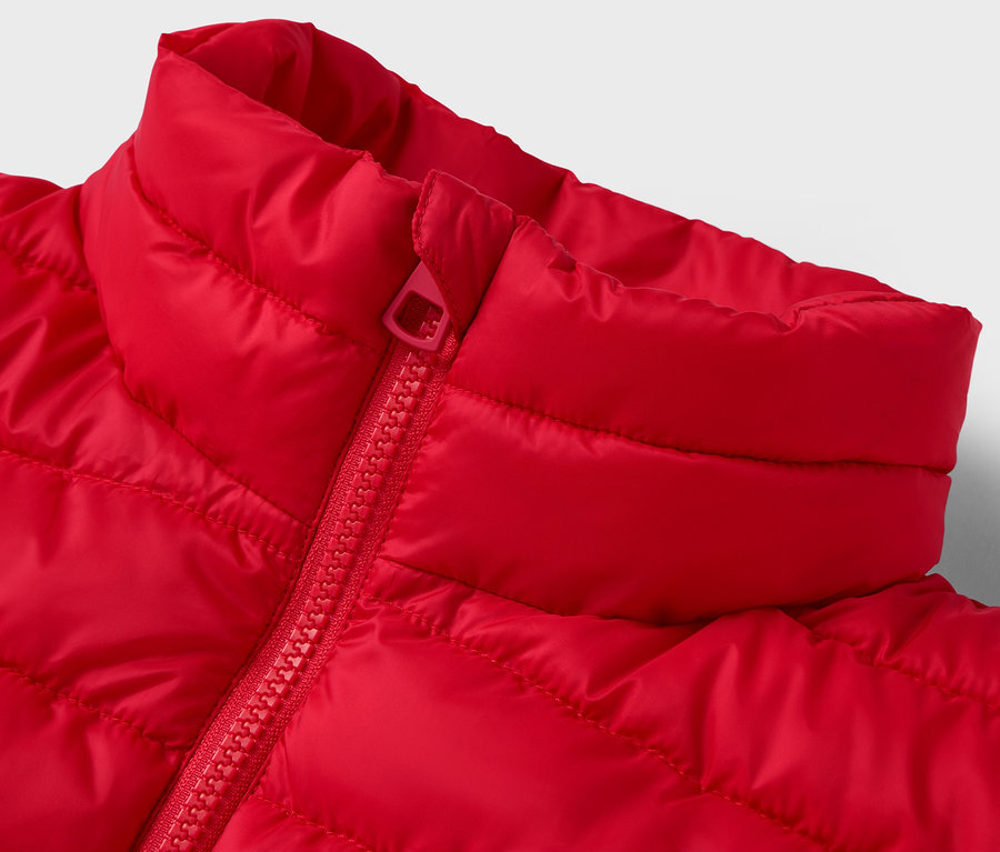 Detail červené prošívané bundy s límcem a zipem.