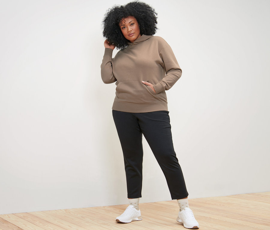 Žena pózuje v béžové mikině s kapucí.