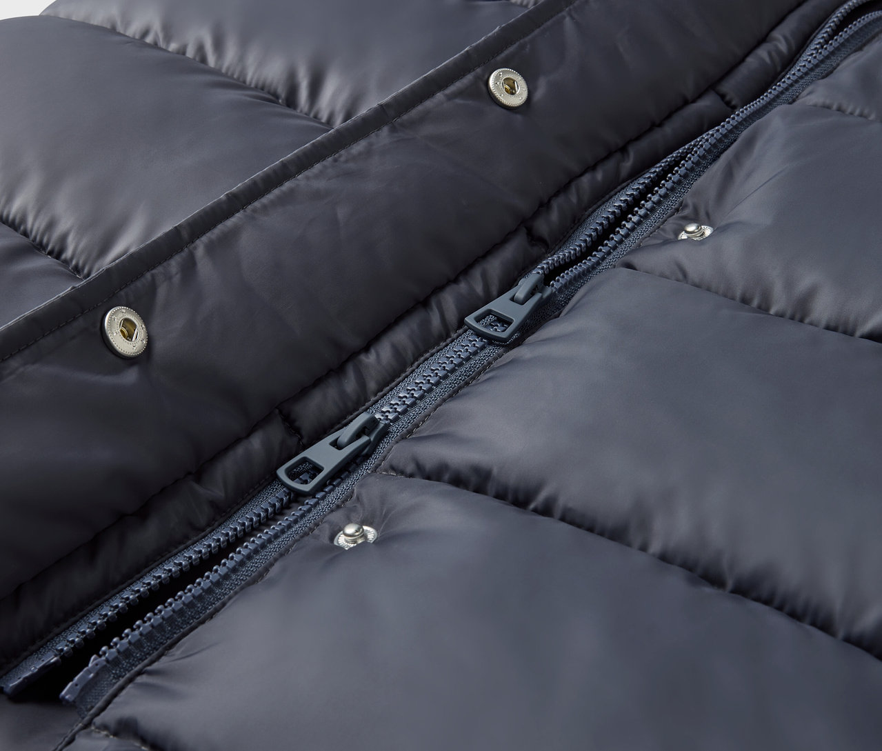 Detail modré prošívané bundy se stříbrnými patentkami a zipem.